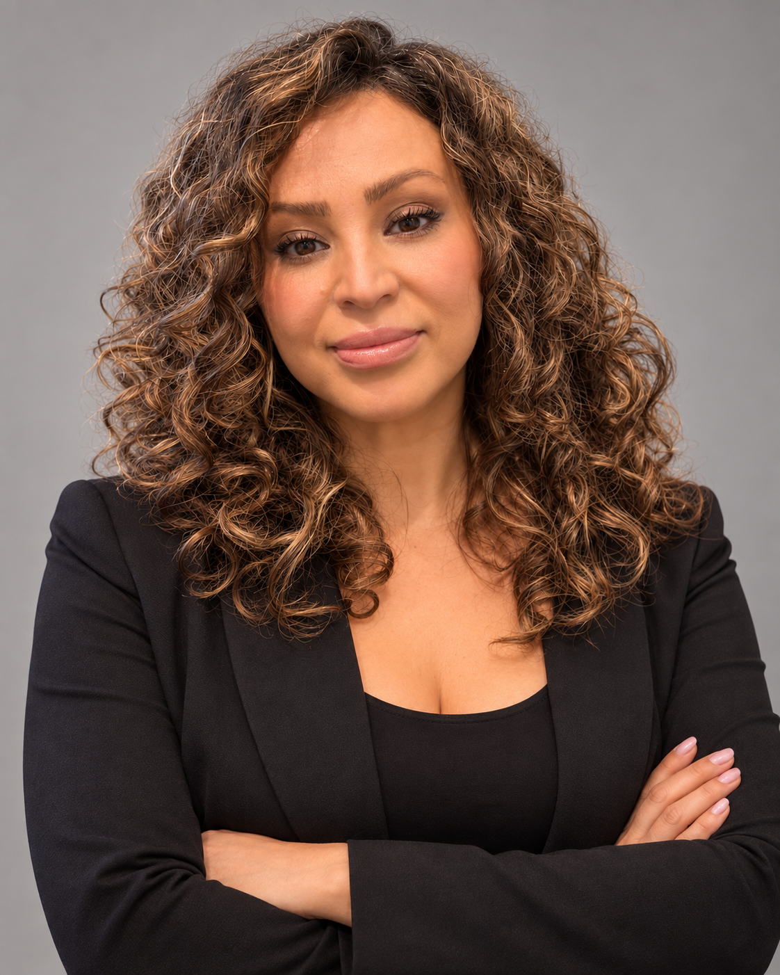Professional portrait of Tammy B. Davila with highlighted brunette curls, a black blazer, and arms crossed